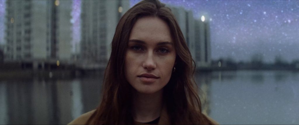 Woman looks in the camera, while the stars are super visible in the sky
