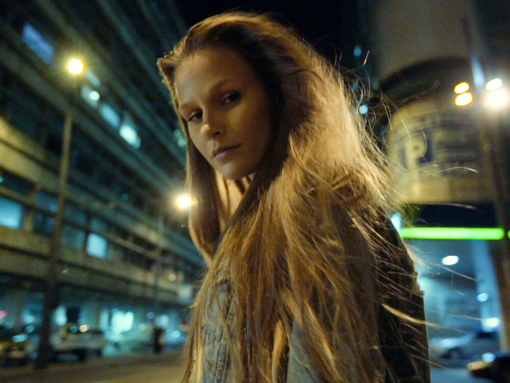 Woman looks down at camera in a bright night scene