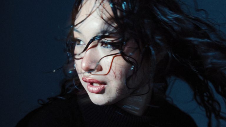 Woman with wet, windswept dark hair and a septum ring in cold blue light, from the fashion film BLUE